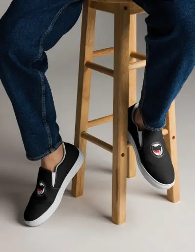 Step into activism with our Antifascist Action Men’s Slip-on Canvas Shoes. These sleek black shoes feature the iconic Antifa design, making a bold statement wherever you go. With elastic side accents for easy wear, a breathable lining keeps your feet comfortable all day long. The soft insole adds extra cushioning.